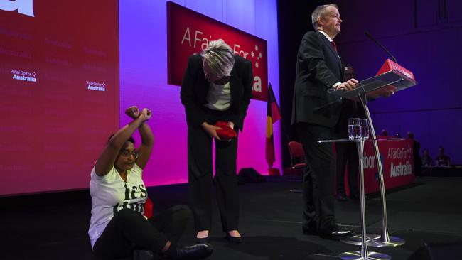 An anti-Adani mine protester sits on stage as Opposition Leader Bill Shorten speaks during day one of the Labor Party national conference in Adelaide. Picture: AAP / Lukas Coch