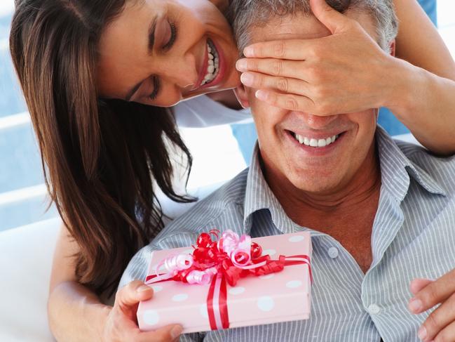 Pretty woman covering her husbands eyes to surprise him with a gift. Couple. Generic image.