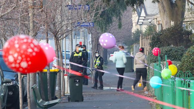 Police walk past balloons that have been tied to the fence at the North Melbourne towers. Picture: David Crosling