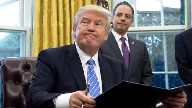 TOPSHOT - US President Donald Trump signs an executive order as Chief of Staff Reince Priebus looks on in the Oval Office of the White House in Washington, DC, January 23, 2017. Trump on Monday signed three orders on withdrawing the US from the Trans-Pacific Partnership trade deal, freezing the hiring of federal workers and hitting foreign NGOs that help with abortion. / AFP PHOTO / SAUL LOEB