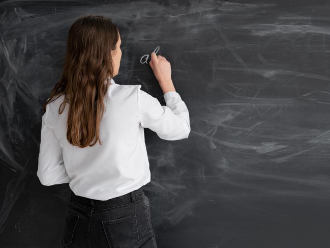 student woman or teacher in the class writes math formulas in chalk on a black chalkboard. young girl stands with her back to the camera. Back to school. Education concept. Banner. Place for your text