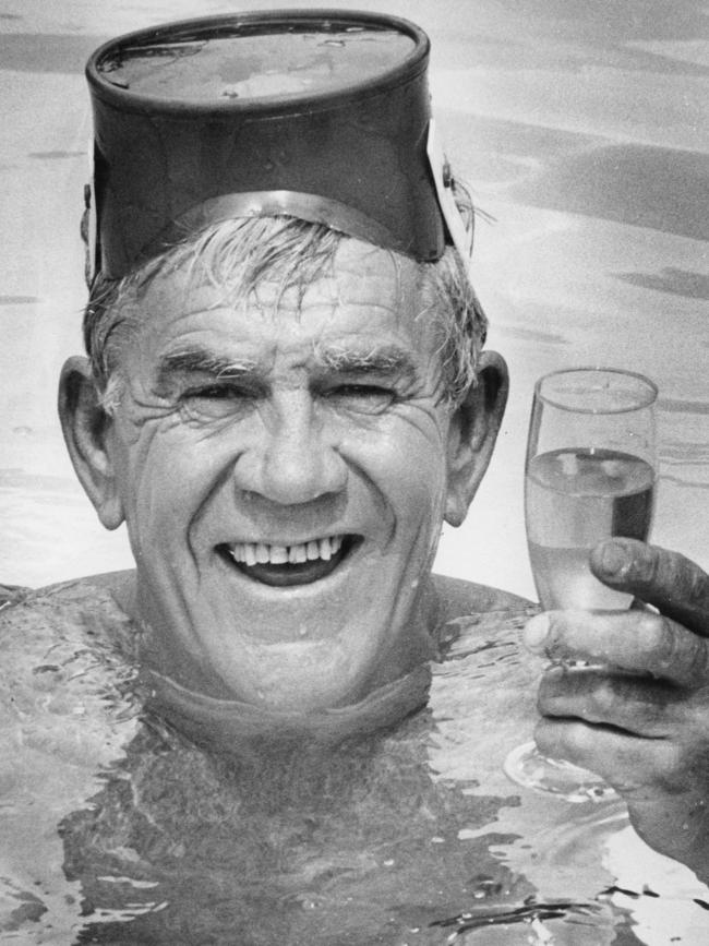 1982. Lou Richards in a swimming pool with a drink.