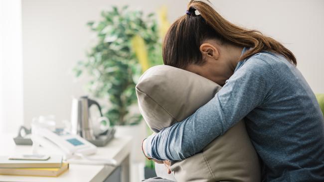 Unhappy lonely depressed woman at home, she is sitting on the couch and hiding her face on a pillow, depression concept