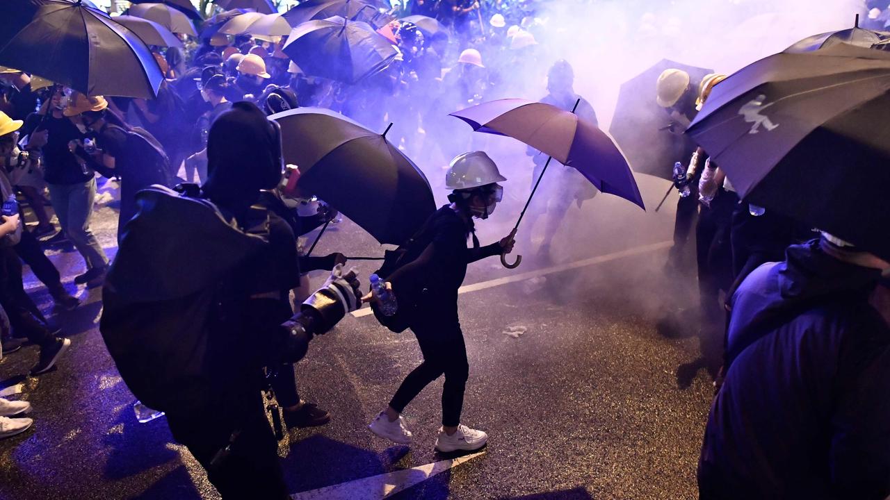 Protesters hold umbrellas as they are enveloped by tear gas on a street during a demonstration against the bill.