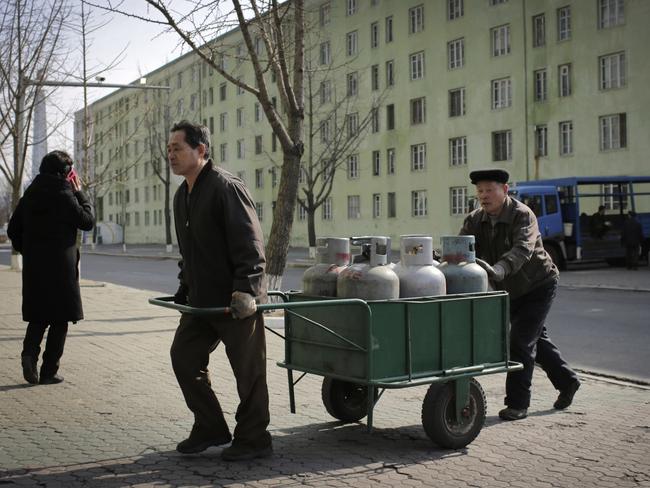 Men transport gas cylinders as they pass a woman talking on a mobile phone near an apartment block at the start of a work week in Pyongyang, North Korea. Picture: AP