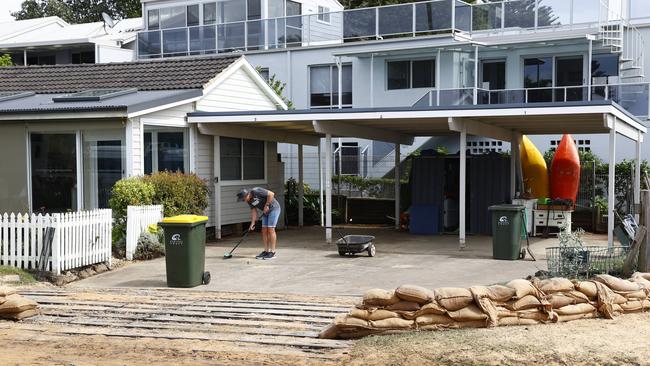 A man cleans up and arranges sandbags in front of his house at Avoca Beach on the Central Coast on Sunday. Picture: Richard Dobson