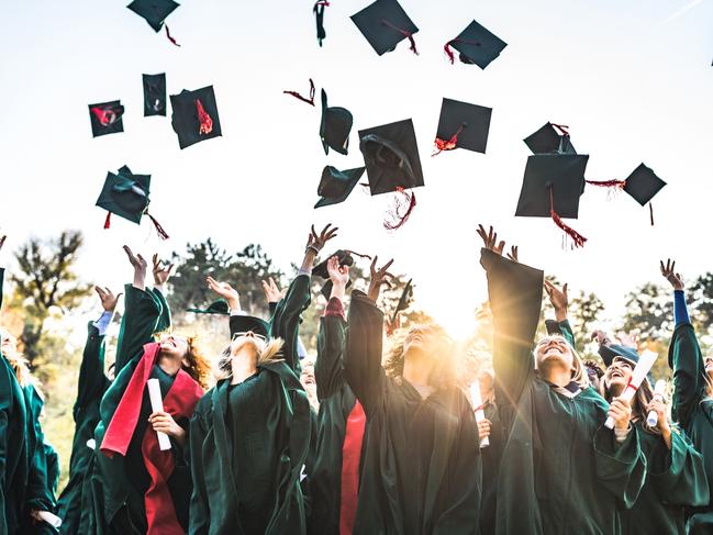 Large group of happy college students celebrating their graduation day outdoors while throwing their caps up in the air.