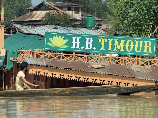 A boatman rows past a damaged and partially-sunken houseboat on Dal Lake.