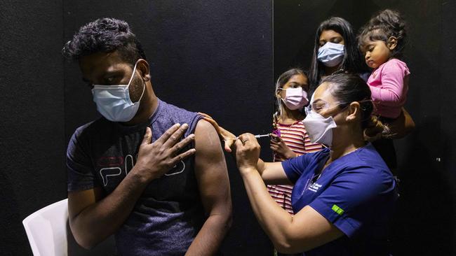 Manjula Gamageat receives a Pfizer vaccination while his family looks on in a pop-up vaccination hub at Casey Fields in Cranbourne. Picture: Daniel Pockett