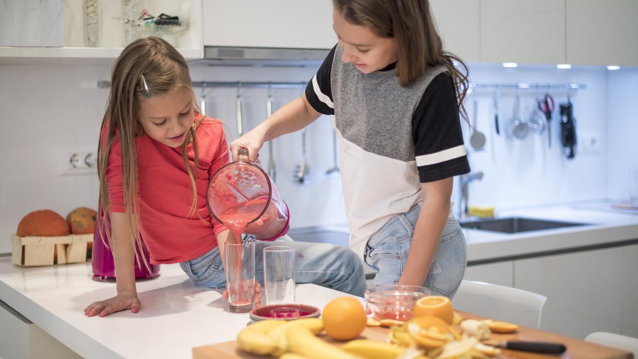 Two little girls preparing a smoothie in the kitchen