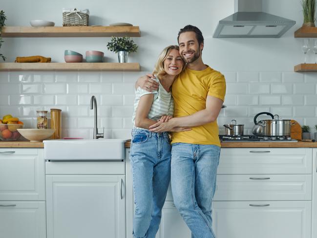 Full length of young couple embracing while standing at the domestic kitchen