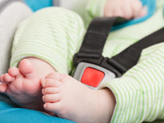 Little smiling baby child fastened with security belt in safety car seat