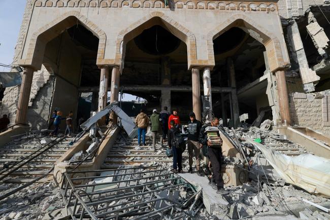 A man walks with salvaged religious books among the rubble of a mosque following Israeli bombardment in Rafah