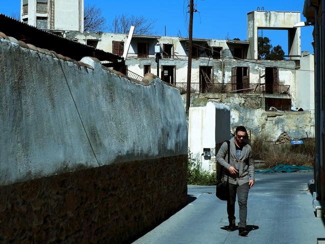 In this Thursday, March 10, 2016 photo, a man walks at the old city in front of an abandoned building at the UN buffer zone controlled area that divides the north form the south in the divided capital Nicosia, Cyprus. Tiny Cyprus heads into this week’s European Union-Turkey summit facing intense pressure to unblock rival Turkey’s EU membership talks and pave the way for a crucial deal to control the inflow of migrants and preserve the fractured bloc’s unity. But the stakes are high for the ethnically-split island nation too; giving in without clinching substantial trade-offs could undermine reunification talks with breakaway Turkish Cypriots and damage the presidency of Nicos Anastasiades. (AP Photo/Petros Karadjias)