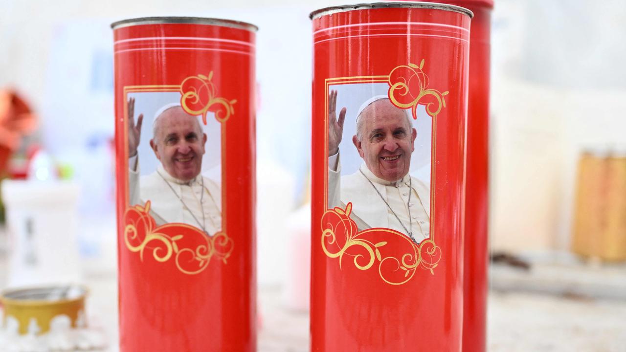 Candles depicting Pope Francis are placed in front of the statue of John Paul II outside the Gemelli hospital where Pope Francis is hospitalised, in Rome on February 24, 2025. (Photo by Alberto PIZZOLI / AFP)