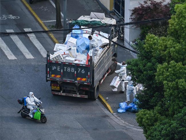 Workers wearing personal protective equipment (PPE) load empty boxes onto a truck next to the entrance of a neighbourhood during a coronavirus lockdown in Shanghai. Picture: AFP