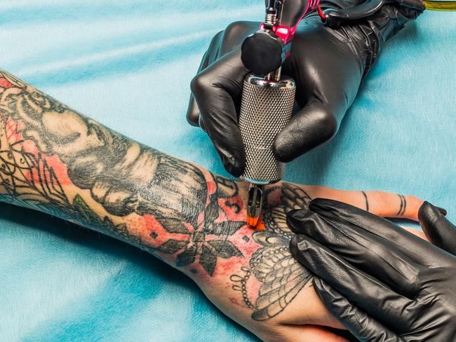 Close up tattoo artist demonstrates the process of getting black and red tattoo with orange paint. Master works on the professional blue mat in black sterile gloves.  - Picture istock