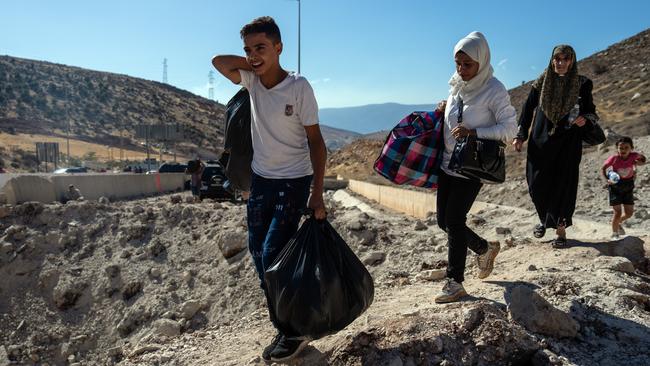 People carry baggage around the crater from an Israeli air strike as they make their way across the border from Lebanon into Syria on October 5. Picture: Carl Court/Getty Images *** BESTPIX ***