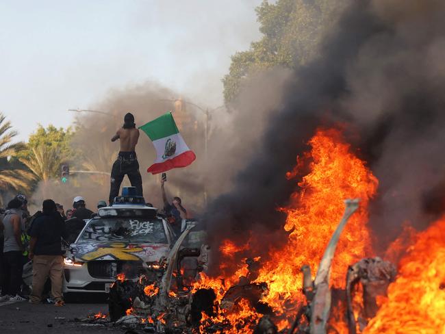 LOS ANGELES, LOS ANGELES - JUNE 08: (EDITORS NOTE: Image contains profanity) Burning cars line a street as people protest on June 08, 2025 in Los Angeles, California. Tensions in the city remain high after the Trump administration called in the National Guard against the wishes of city leaders following two days of clashes with police during a series of immigration raids.   Jim Vondruska/Getty Images/AFP (Photo by Jim Vondruska / GETTY IMAGES NORTH AMERICA / Getty Images via AFP)