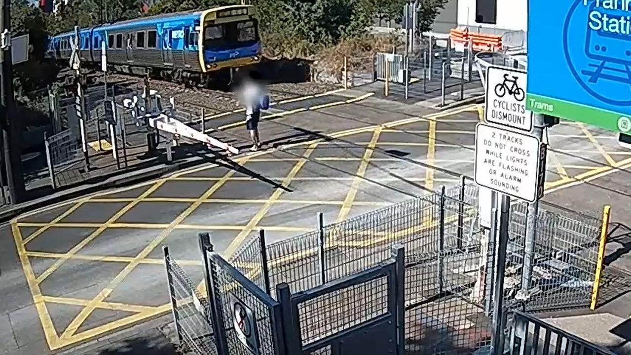 A pedestrian walks into a level crossing as a train approaches Prahran Station early in 2022.