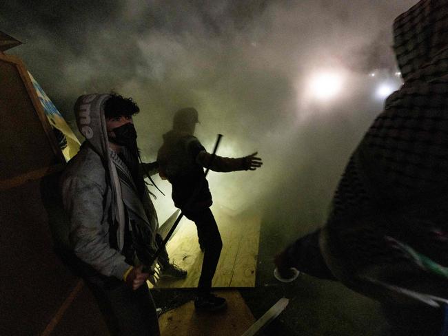 Pro-Palestinian demonstrators engulfed in tear gas regroup and rebuild the barricade surrounding the encampment set up at the University of California Los Angeles as clashes erupt with counter protesters. Picture: AFP