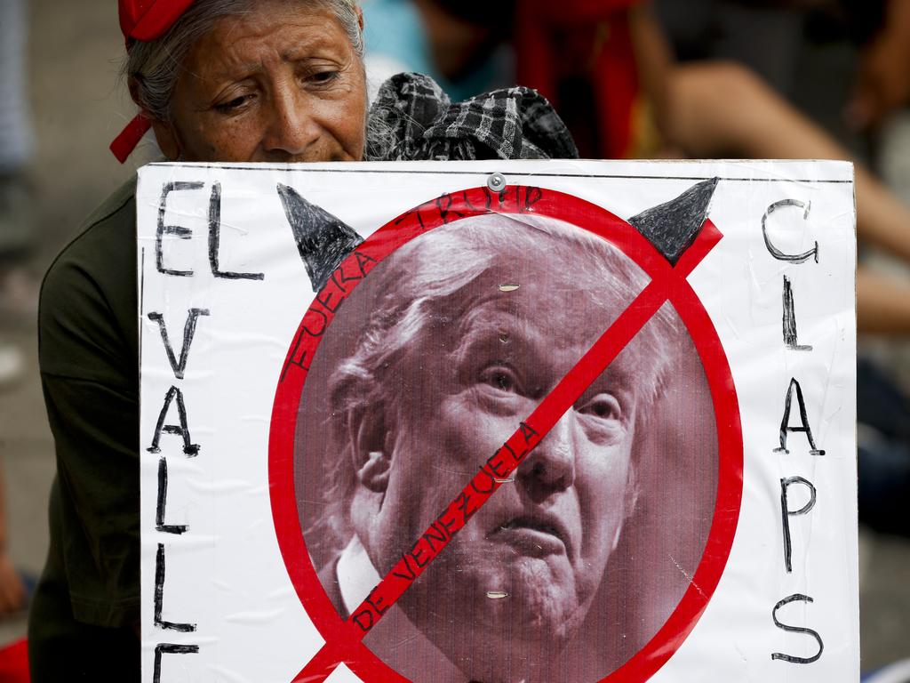 A government supporter holds a poster with a no symbol over an image of US President Donald Trump defaced with devil horns, and a message that reads in Spanish: "Stay out Venezuela Trump". Picture: AP