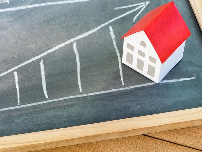 Graph representing the rise in mortgage interest rates drawn on a chalkboard lying on a wooden table. A model of a house with a red roof is on the chalkboard. Finance and real estate concept.