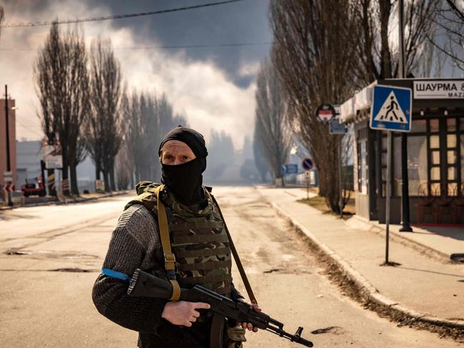 A Ukrainian serviceman stands guard near a burning warehouse hit by a Russian shell in the suburbs of Kyiv. Picture: AFP