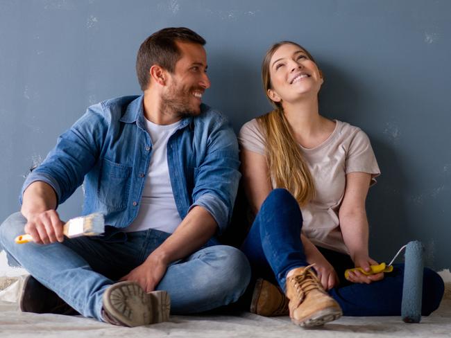 Loving Latin American couple having fun renovating their house and painting the walls and smiling while taking a break - home improvement concepts