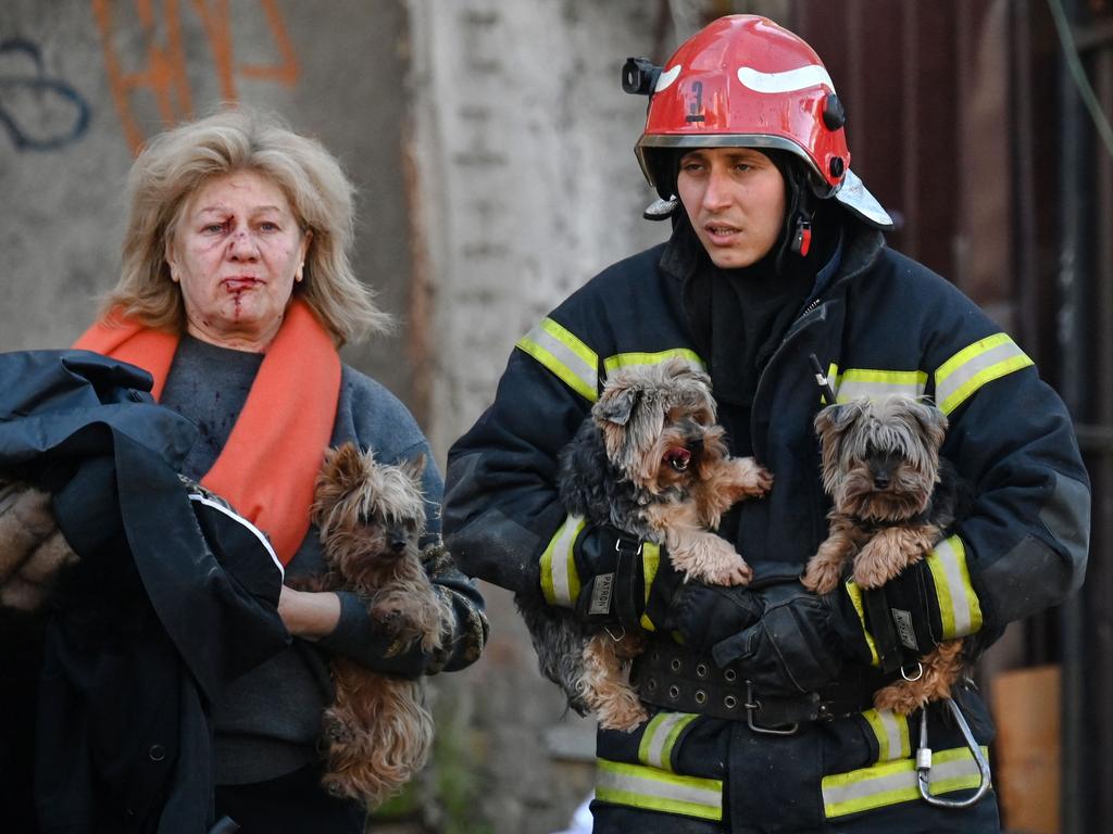 An emergency worker carries dogs as he escorts a local resident outside a partially destroyed multistorey office building in Kyiv. Picture: AFP