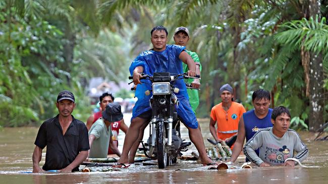 Residents navigate floodwaters with a makeshift raft and motorcycle in Prosperidad, Philippines after heavy rains. Picture: Erwin Mascarinas/AFP