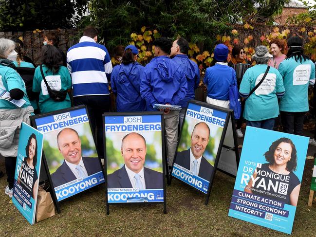 Political party volunteers handout how-to-vote cards while people queue at a pre-polling centre in Melbourne on May 17, 2022 as independent candidate Monique Ryan takes on Australia's treasurer Josh Frydenberg in his usually safe seat of Kooyong in the May 21 general election. (Photo by William WEST / AFP)