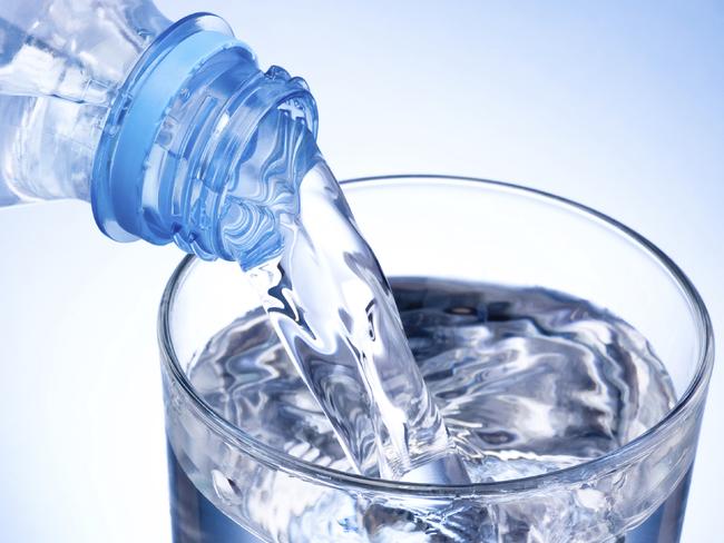 Close-up Pouring glass of water from a plastic bottle on blue background