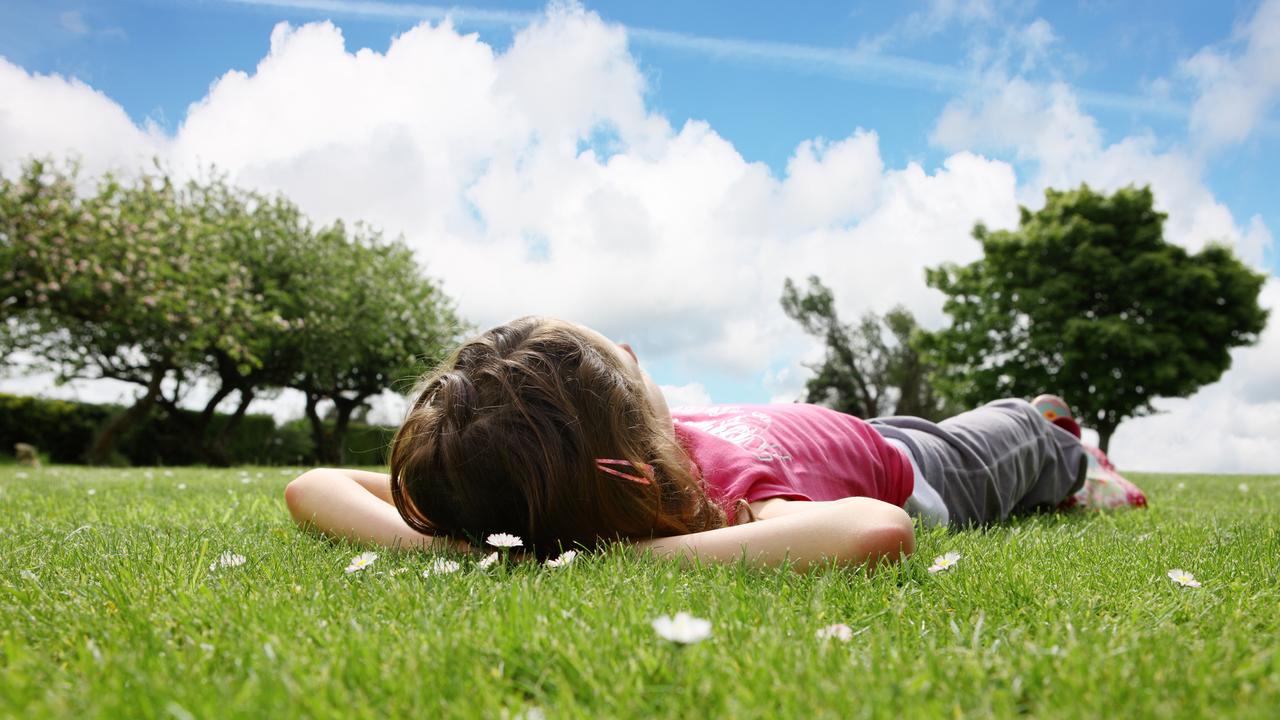 Child lying in the grass looking at clouds.