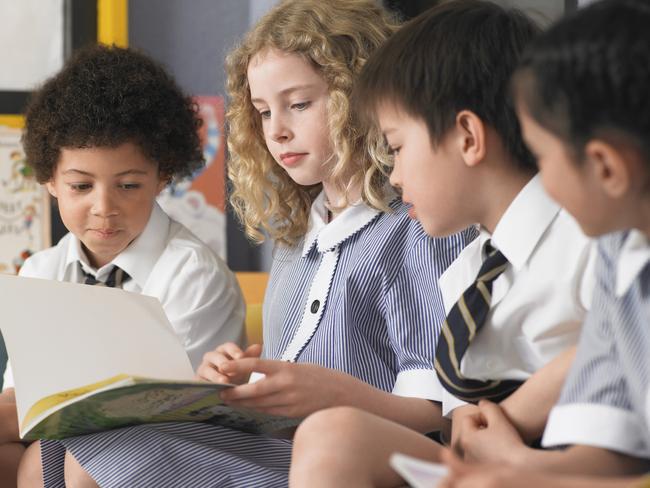 Row of elementary students reading book sitting in classroom