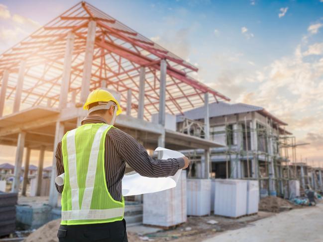 Developing Queensland - Professional engineer architect worker with protective helmet and blueprints paper at house building construction site background.