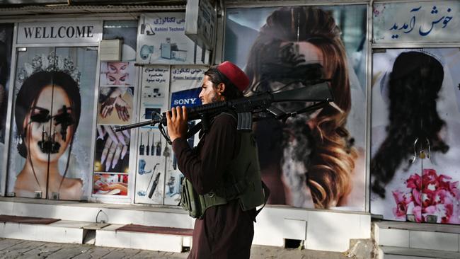 A Taliban fighter walks past a beauty saloon with images of women defaced using a spray paint in Shar-e-Naw in Kabul. Picture: Wakil Kohsar/AFP