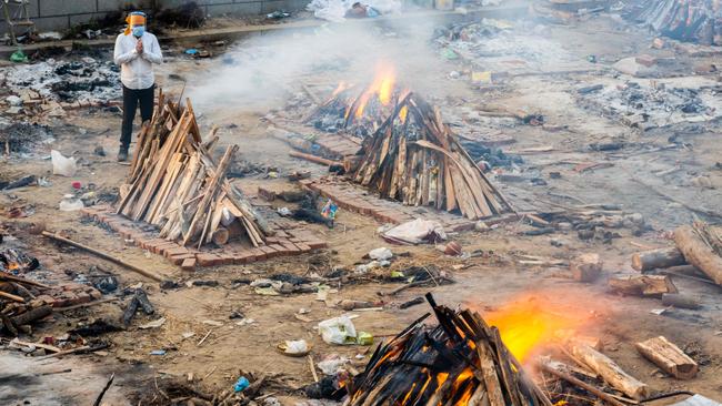 A man prays next to a burning pyre of a victim who died of the Covid-19 coronavirus at a cremation ground in New Delhi on April 26, 2021. (Photo by Jewel SAMAD / AFP)