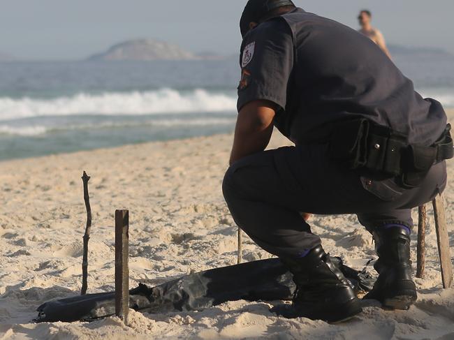 RIO DE JANEIRO, BRAZIL - JUNE 29: A police officer kneels over a body part, covered in a plastic bag, which was discovered on Copacabana Beach near the Olympic beach volleyball venue on June 29, 2016 in Rio de Janeiro, Brazil. Parts of a mutilated body were discovered on the sands of the beach while it remains unknown how the person died. The Rio 2016 Olympic Games begin August 5 amidst an economic crisis in the country. (Photo by Mario Tama/Getty Images)