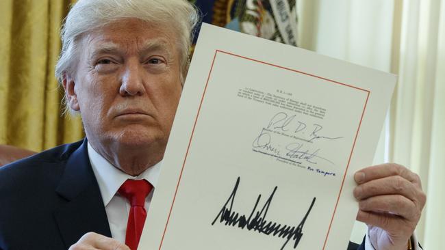 President Donald Trump shows off the tax bill after signing it in the Oval Office of the White House, Friday, Dec. 22, 2017, in Washington. (AP Photo/Evan Vucci)