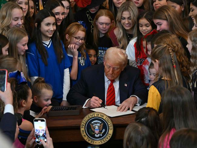 President Trump signs the executive order surrounded by young girls. Picture: AFP