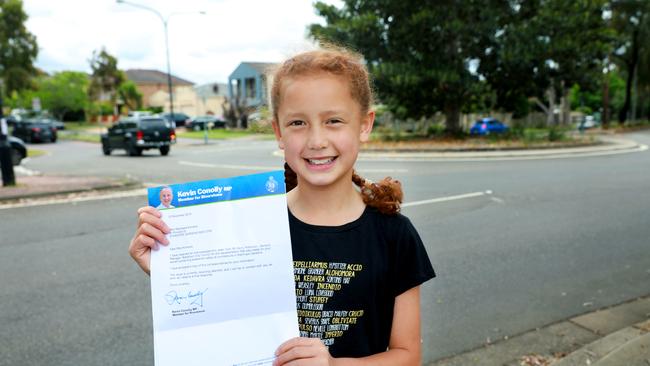 Mackaela Komene, 11, with her letter, next to the road she crosses to get to school.