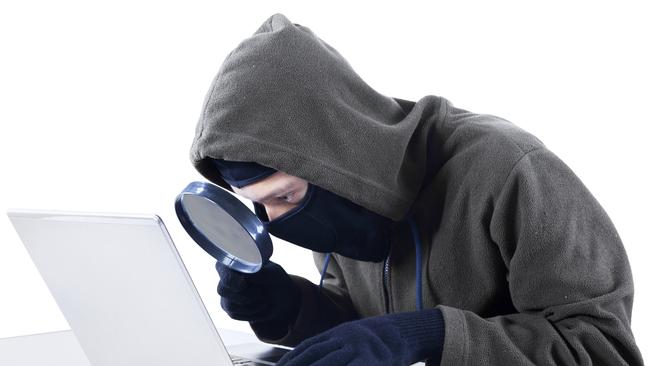 Internet Theft – a hooded man looking at computer screen using magnifying glass; scams, scammer, fraud generic