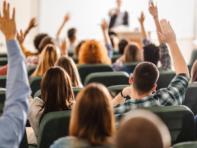 Back view of college students raising their arms on a class at lecture hall.