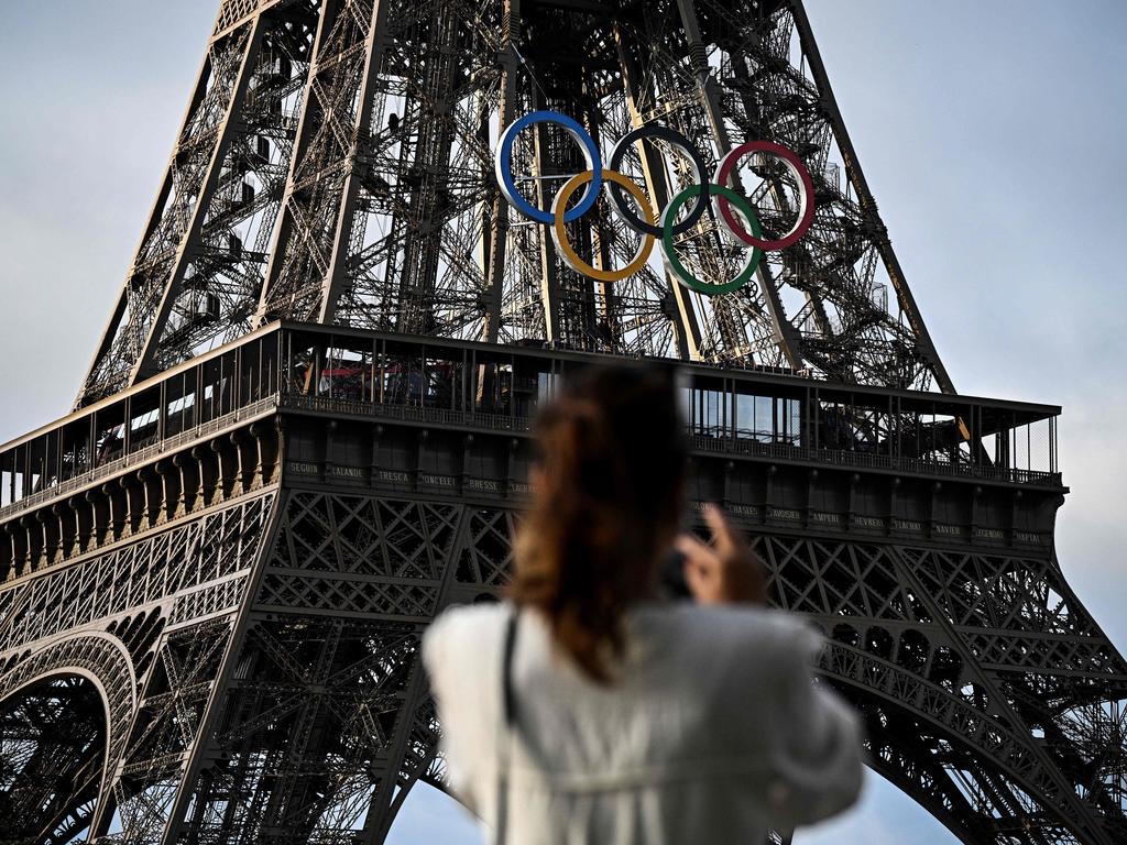 A woman takes a picture of the Eiffel Tower decorated with the Olympic rings for the upcoming Paris 2024 Olympic Games, in Paris, on June 17, 2024. (Photo by JULIEN DE ROSA / AFP)