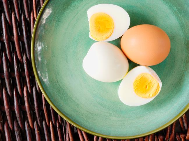 Hard-boiled egg cut and piled on egg slicer and full egg with shell on green plate or dish.