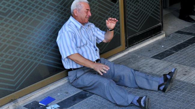 A distressed pensioner sits on the ground outside a national bank branch, as banks opened only for pensioners to allow them to withdraw their pensions, with a limit of 120 euros, in Thessaloniki, on July 3, 2015. Greece is almost evenly split over a crucial weekend referendum that could decide its financial fate, with a 'Yes' result possibly ahead by a whisker, the latest survey Friday showed. Prime Minister Alexis Tsipras's government is asking Greece's voters to vote 'No' to a technically phrased question asking if they are willing to accept more tough austerity conditions from international creditors in exchange for bailout funds. AFP PHOTO /SAKIS MITROLIDIS