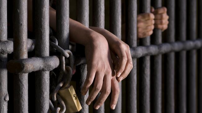 Close up of hands, behind the bars of a prison. Istock