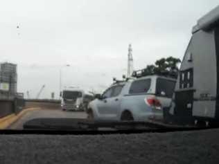 A motorist towing a caravan overtakes a stationary vehicle towards an oncoming truck crossing double lines to navigate the infamous bend on the Grafton Bridge.