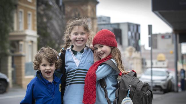 Finn Zabel 5, Lottie Zabel 7 and Esther Kelly 6 take shelter while waiting for the bus at North Hobart. Picture: Chris Kidd